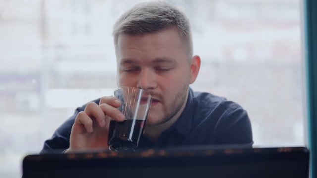 A young freelancer working on a laptop and drinking juice in the background of a winter window