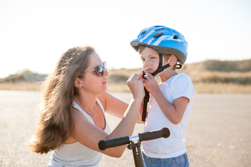 Fototapeta premium handsome young mother helps to her cute little son put on sport helmet