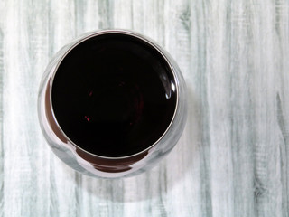 Glass of red wine on a light wooden table, top view