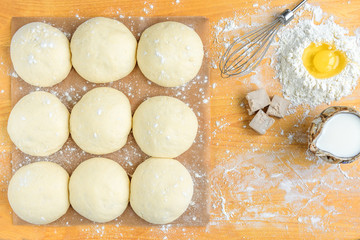 Baking background top view. Making sweet bun or bread dough. Cooking ingredients for pastry on wooden board with dough, egg, yeast, milk, flour. Culinary classes or recipe concept.