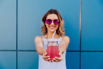 Cheerful attractive girl holds a jar with cold fruit smoothie, wearing stylish sunglasses. Outdoors. © Maksym Azovtsev