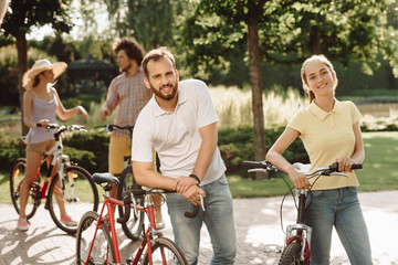 Young smiling peope with bicycles outdoors. Young happy couple of cyclists looking at camera on summer nature background.