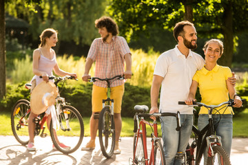Young cheerful tourists with bicycles outdoors. Happy couple riding bicycle in the park. Summer travel concept.