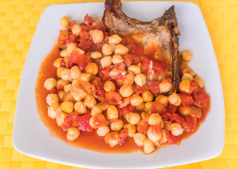 pork chop with a chickpea and tomato, with garlic and onion sauce on a square white plate and yellow place mat