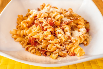 Pasta spirals with salami and tomato in a white dish on a yellow place mat