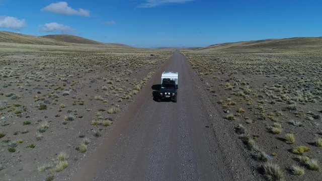 Aerial drone scene of van and trailer, motorhome in steppe, patagonia argentina riding on a gravel lonely road. Tromen volcano National Park. Camera moving backwards tracking car.