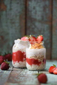 Tasty nutritious summer breakfast. Overnight raw oatmeal in jars with shabby organic strawberries on shabby turquoise background