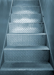 grey steel industrial staircase with rough patterned grip texture in a passage between two metal plate walls