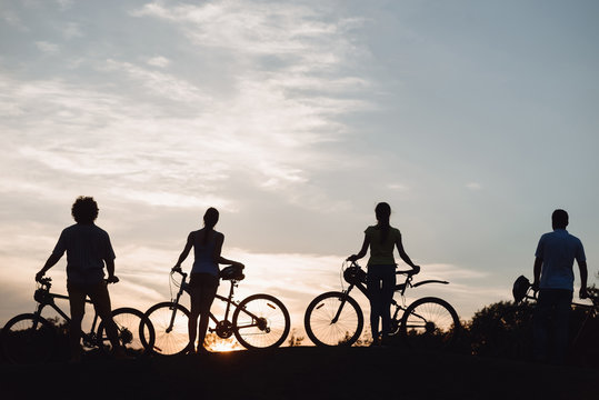 Four young cyclists at beautiful sunset. Silhouettes of young people with bicycles at amazing sunset. Enjoying the nature.