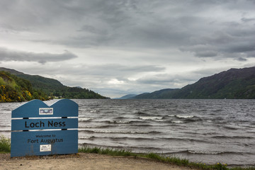 Fort Augustus, Scotland - June 11, 2012: Choppy dark gray Loch Ness with surf at Fort Augustus with sign under heavy cloudscape. Hills on horizon.