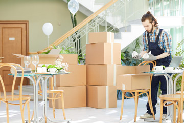 Concentrated handsome young logistics company mover in uniform unpacking box and checking cups while working at place of delivery