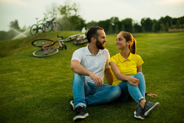 Young beautiful couple sitting on grass in the park. Romantic couple on sunny meadows. Happy summer weekend together outdoors.