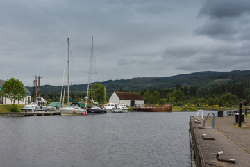 Fort Augustus, Scotland - June 11, 2012: Oich Canal behind the locks. Dock on side has pleasure boats moored, Green hils on horizon under heavy gray sky.
