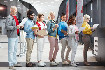 Serious pensive people in casual clothing reading application form while standing in line while...