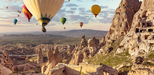 Naklejka premium Balony powietrzne nad tureckim parkiem narodowym w Göreme. Panorama Cappadocia krajobraz - wielo- barwioni balony lata nad halną doliną antyczny jaskini miasteczko Uchisar.