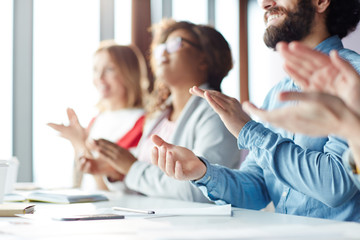 Close-up of cheerful business people sitting in row at table and applauding speaker after presentation during educational conference
