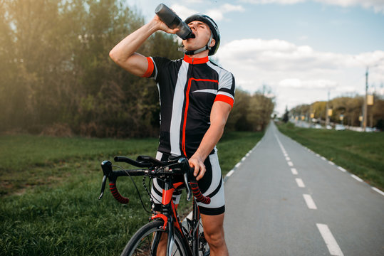 Male bycyclist drinks water while training