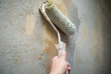 Close-up hand holds rolling paint brush, painting interior stucco wall with white color.Preparation...