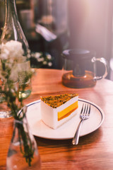 Piece of raw vegan mango coconut cake on wooden table at the restaurant. Food photography concept. Warm tones filter effect, vertical