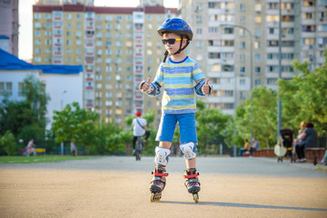 Little boy riding on rollers in the summer in the Park. Happy child in helmet learning to skate