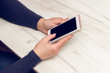 Female hands hold a smartphone over a wooden table