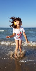 bambina che ascolta la musica con le cuffie in riva al mare e salta