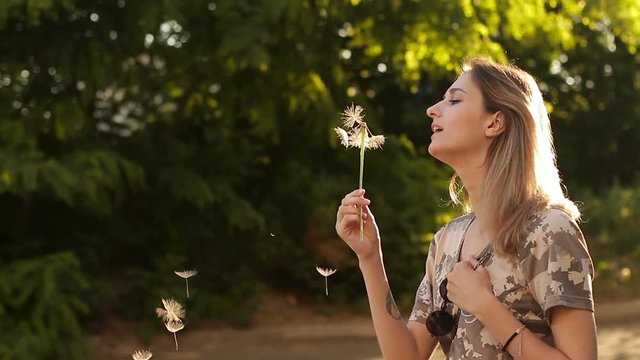 Young beautiful girl blowing out a huge dandelion