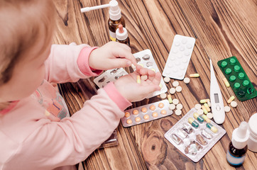 Children's hands with medicines on a wooden table. A small child left unattended plays dangerous drugs