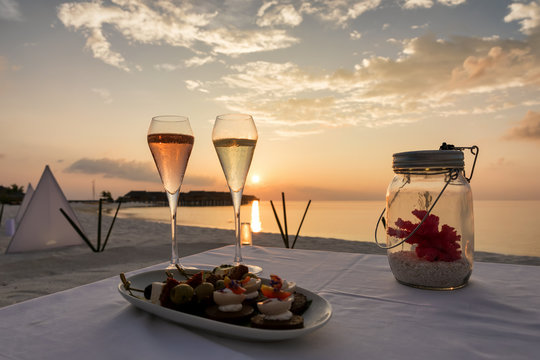 Sektgl&auml;ser mit Kanapees am tropischen Strand zum Sonnenuntergang im Resort Hotel auf den Malediven
