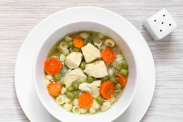 Homemade chicken soup with pea, carrot and small shell pasta in bowl, photographed overhead with natural light (Selective Focus, Focus on the top of the soup)