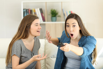 Amazed girl interrupting her friend to watch tv