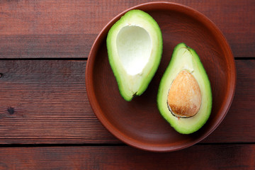 Avocado on a wooden background, two halves of avocado on a clay plate, tropical fruit in retro...