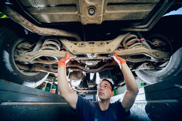 Car mechanic examining car suspension of lifted automobile at repair service station