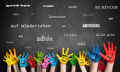 Viele Kinderhände vor Wandtafel mit dem Wort "Auf Wiedersehen" in vielen Sprachen 