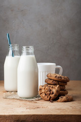 Two bottles of milk and chocolate chip cookies on dark background with copy space