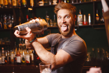 Joyful bartender mixes a cocktail in a shaker