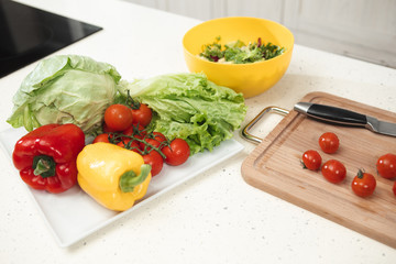 Close up of fresh vegetables on table. Tomatoes, peppers and cabbage with lettuce on tray near wooden board and knife 
