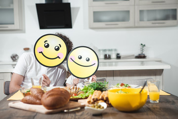We like healthy food. Portrait of happy father and daughter having lunch together at home. They are sitting at table and holding positive smiles near their faces 