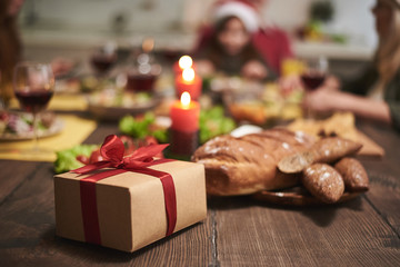 Focus of gift with red ribbon put on wooden board full of festive dishes. Box and candles creating festive atmosphere for dinner