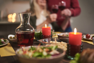 Obraz na płótnie Canvas Focus of candles lit on festive dinner. There are red wine and variable dishes on table creating romantic atmosphere for couple on background 