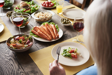 Close up of mature female sitting at table. She is having salad and red wine. Wooden board is full of tasty dishes