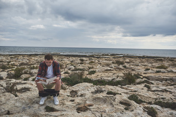 Dreaming of summer resort. Pensive young man is reading magazine while sitting on toilet bowl. He is imaging that he is at the seaside. Copy space 