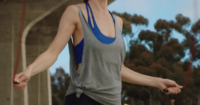 Slow motion shot of athletic woman exercising outside jump roping in urban environment on sunny day