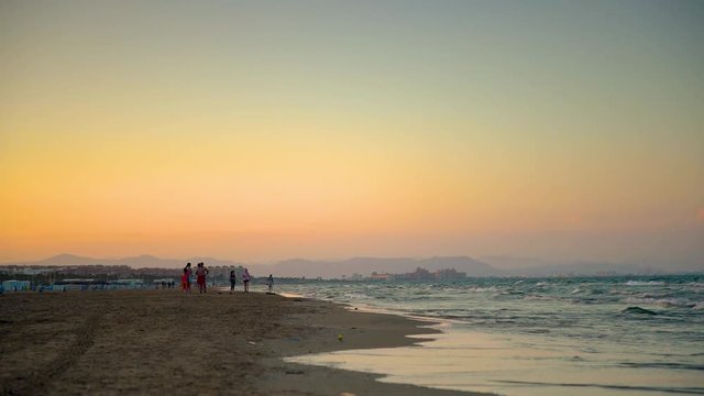 Light waves and people gather after swimming in front of the sunset on the beach of Malvarros. Valencia, Spain