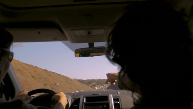 Woman driving a car while a man looks at his phone and points ahead