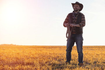 A man cowboy hat and a loso in the field. American farmer in a f