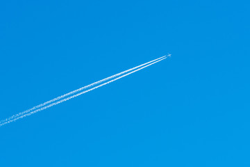 The aircraft in the blue sky. The airplane leaves behind a white condensation trail or inversion...
