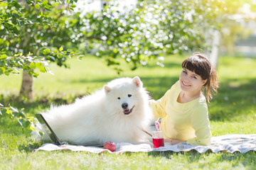 A brunette girl with a white dog on nature. The girl and the big dog lie on the grass in the city park.