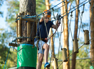 cute young boy on tree tops in the amusement rope pak in the summer on the holidays