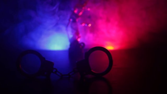 Legal law concept. Silhouette of  handcuffs with The Statue of Justice on backside with the flashing red and blue police lights at foggy background. Slider shot